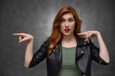 Stüdyoda gri arka planda farklı duyguları olan güzel bir aktris. Siyah ceketli, uzun kızıl saçlı beyaz bir kadının stüdyo fotoğrafı..