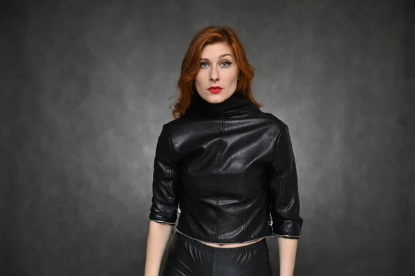 Pretty model actress posing with different emotions on a gray background in the studio. Portrait of a young caucasian woman with long red hair in a green t-shirt and a black jacket.