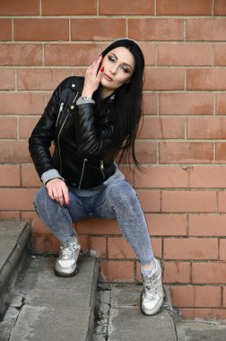 Bina duvarına karşı poz veren bir model. Güneşli havada uzun bir portre. Beyaz tenli, esmer bir kız. Harika bir vücudu var..