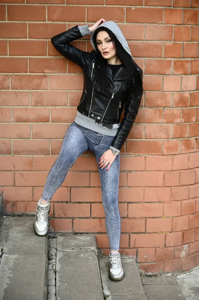 Model posing against the backdrop of a building wall. Full-length portrait in sunny weather outdoors caucasian brunette girl with a great figure.