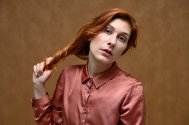Beyaz, sakin, pembe tişörtlü, uzun kızıl saçlı güzel bir kadının bej arkaplanda resmi. Stüdyo çekimlerinde bile duygular.