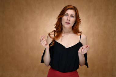 Model aktris kamerada konuşurken farklı duygular gösterir. Siyah bluzlu, bej arka planda uzun kızıl saçlı beyaz bir kadının stüdyo fotoğrafı..