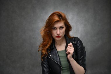 Siyah ceketli, uzun kızıl saçlı, beyaz bir kadının stüdyo fotoğrafı. Stüdyoda gri bir arka planda farklı duyguları olan güzel bir aktris..