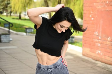 Bahar havasında çekilen fotoğraf, zayıf vücutlu beyaz tenli esmer bir kız zevkle poz veriyor. Fitness modeli şehir parkının arka planına karşı duruyor..