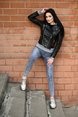 Bina duvarına karşı poz veren bir model. Güneşli havada uzun bir portre. Beyaz tenli, esmer bir kız. Harika bir vücudu var..