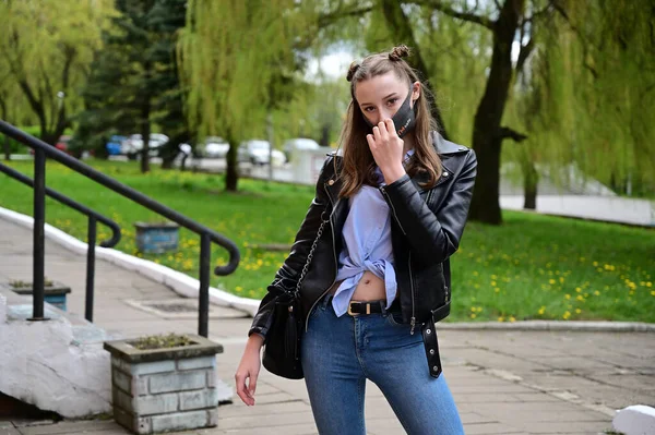 模特儿站在城外的春天公园里 照片上的一个年轻漂亮姑娘戴着防毒面罩 穿着黑色夹克和牛仔裤 — 图库照片