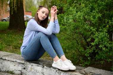 Şehirdeki bahar parkında poz veren bir model. Mavi gömlekli ve kot pantolonlu güzel bir kızın fotoğrafı..