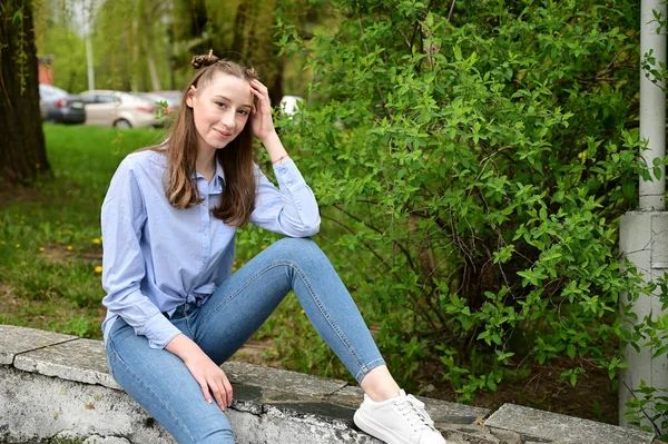 Şehirdeki bahar parkında poz veren bir model. Mavi gömlekli ve kot pantolonlu güzel bir kızın fotoğrafı..