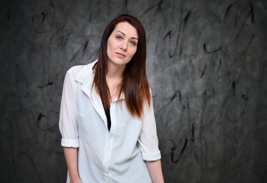 Beyaz gömlekli, gri arka planda duran güzel bir manken. Asgari makyajlı esmer bir kızın stüdyo portresi..