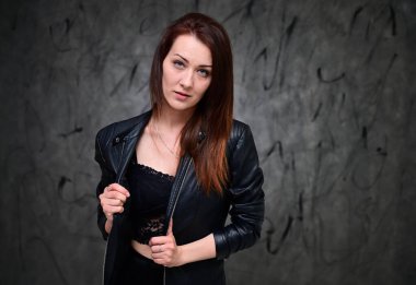 Siyah ceketli, gri bir arka planda duran güzel bir manken. Asgari makyajlı esmer bir kızın stüdyo portresi..