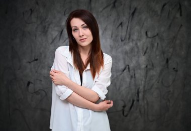 Beyaz gömlekli, gri arka planda duran güzel bir manken. Asgari makyajlı esmer bir kızın stüdyo portresi..