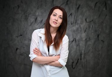 Beyaz gömlekli, gri arka planda duran güzel bir manken. Asgari makyajlı esmer bir kızın stüdyo portresi..