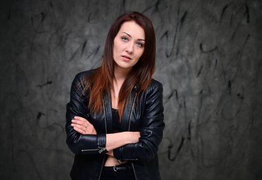 Siyah ceketli, gri bir arka planda duran güzel bir manken. Asgari makyajlı esmer bir kızın stüdyo portresi..