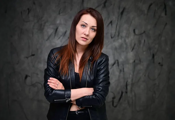 A pretty model is standing on a gray background in a black jacket. Studio portrait of a caucasian brunette girl with minimal makeup.