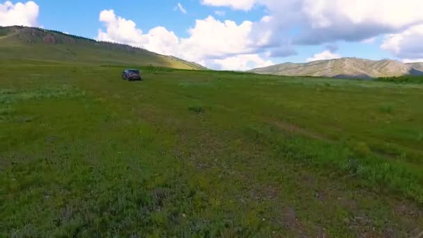 Uma vista do ar para prados verdes, colinas à distância e um carro andando off-road na República de Khakassia. Rússia — Vídeo de Stock