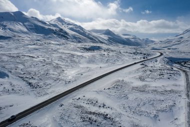 İzlanda 'nın kuzeyindeki karlı dağların arasında dolambaçlı bir yol manzarası.