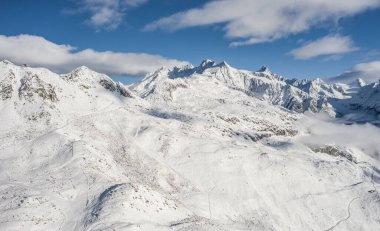 Aletsch Arena bölgesinde taze kar ve bulutlarla kaplı bir ormanın havadan görünüşü. Sonbaharda İsviçre