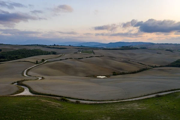 Vista aérea de uma paisagem rural durante o pôr do sol na Toscana. Fazenda rural, ciprestes, campos verdes, luz solar e nuvens. Itália, Europa . — Fotografia de Stock