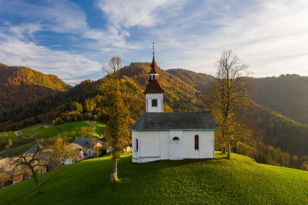 Vista aérea de colinas, floresta colorida e igreja de Sv Tomaz. Pôr do sol na Eslovénia no Outono — Fotografia de Stock