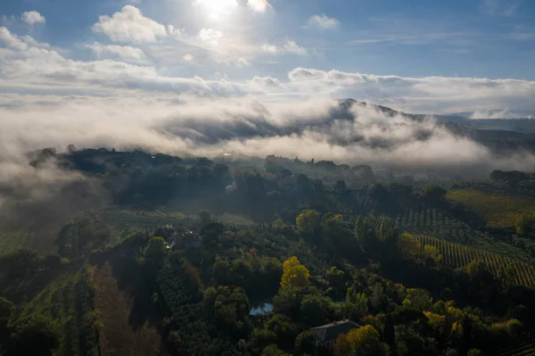 Вид с воздуха на сельский пейзаж во время восхода солнца в Тоскане. Сельская ферма, виноградники, зеленые поля, солнечный свет и туман. Италия, Европа . — стоковое фото