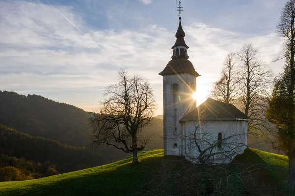 Vista aérea de colinas, floresta colorida e igreja de Sv Tomaz. Pôr do sol na Eslovénia no Outono — Fotografia de Stock