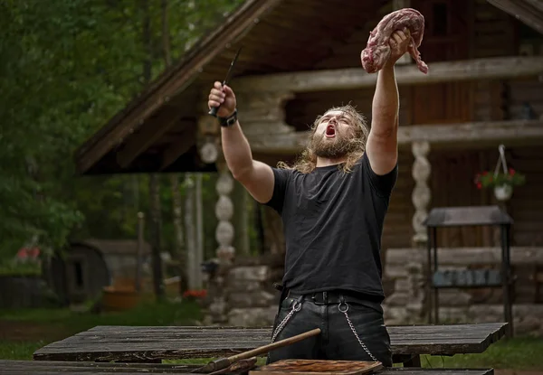 Brutaler Mann mit langen Haaren bereitet Fleisch in der Nähe von Waldhaus zu — Stockfoto