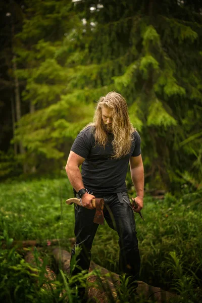 Cabello largo Hombre brutal con hachas en un bosque — Foto de Stock