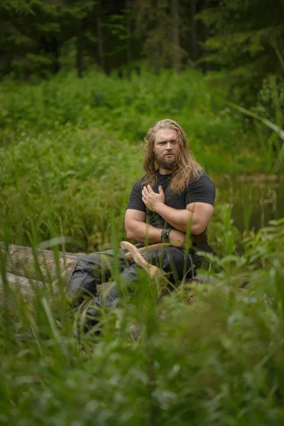 Langhaariger brutaler Mann mit Äxten im Wald — Stockfoto