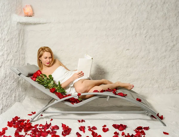 Mujer relajante en la sala de sal con libro, rosas y pétalos —  Fotos de Stock