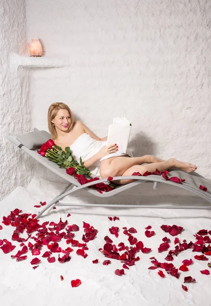 Mujer relajante en la sala de sal con libro, rosas y pétalos — Foto de Stock