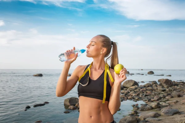 Молодая красивая спортсменка пьет воду на пляже с измерительной лентой — стоковое фото