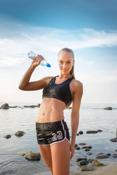 Unga vackra idrottskvinna dricksvatten på stranden — Stockfoto