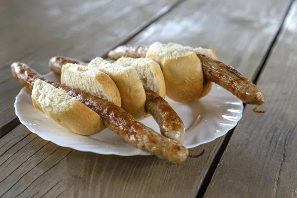 Salsichas nacionais tradicionais grelhadas em pães em uma placa em uma mesa de madeira com foco seletivo no plano do meio — Fotografia de Stock