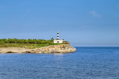 Sakin bir deniz ve mavi gökyüzüne karşı kayalık bir sahilde deniz feneri.