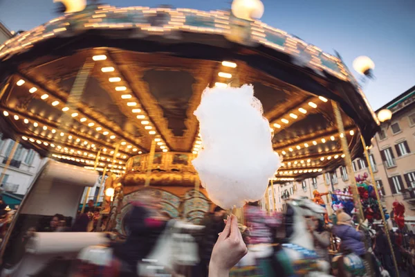 A girl take a cotton candy in front of a carousel horse