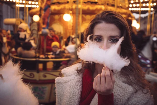 Portrait of a beautiful young girl with white cotton candy in front of a carousel horse