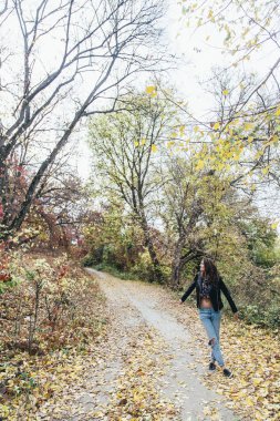 Kız sonbahar parkında yürüyor.