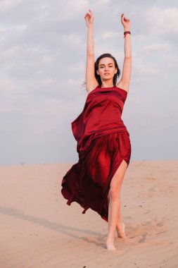 Çölde gün batımında kırmızı bir elbiseyle rüzgârda gelişen bir kız.