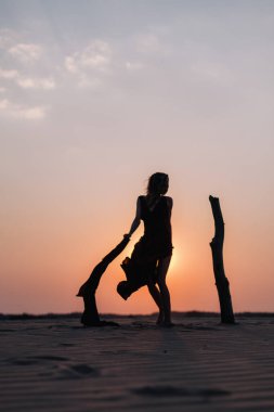 Çölde gün batımında kırmızı bir elbiseyle rüzgârda gelişen bir kız.