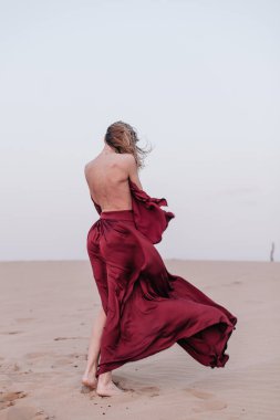 Kumaşlı bir kız çölde rüzgarda duruyor.