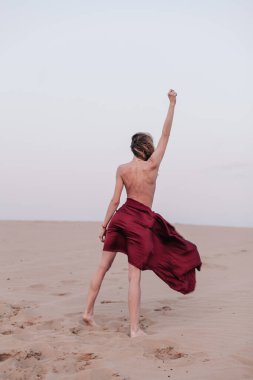 Kumaşlı bir kız çölde rüzgarda duruyor.