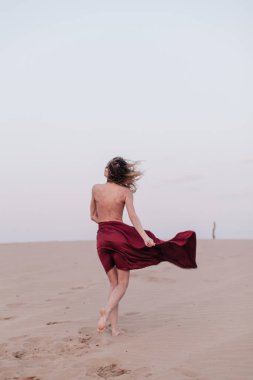 Kumaşlı bir kız çölde rüzgarda duruyor.