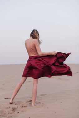 Kumaşlı bir kız çölde rüzgarda duruyor.