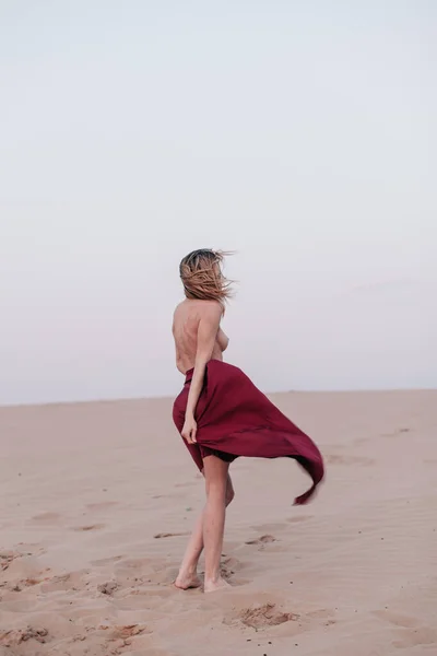 Kumaşlı bir kız çölde rüzgarda duruyor.