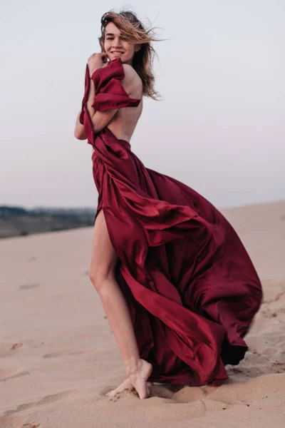 Girl with fabric stands in the wind in the desert