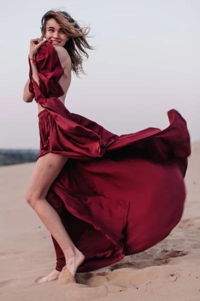 Girl with fabric stands in the wind in the desert