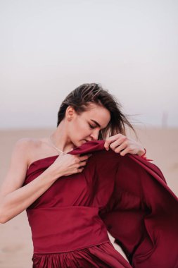 Çölde rüzgarda savrulan kırmızı elbiseli ince bir kızın portresi.