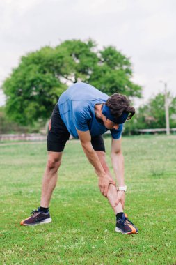Genç adam koşmadan önce stadyumda ısınıyor.