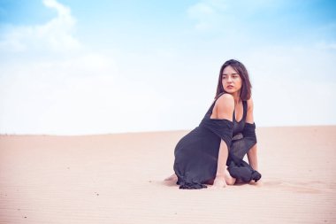 Siyah mayolu bir kız çölde kumların üzerinde oturuyor.
