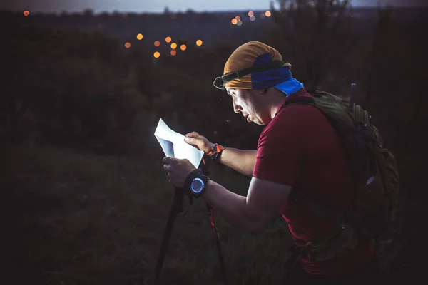 The guy during night orienteering shines a flashlight in a map of the area